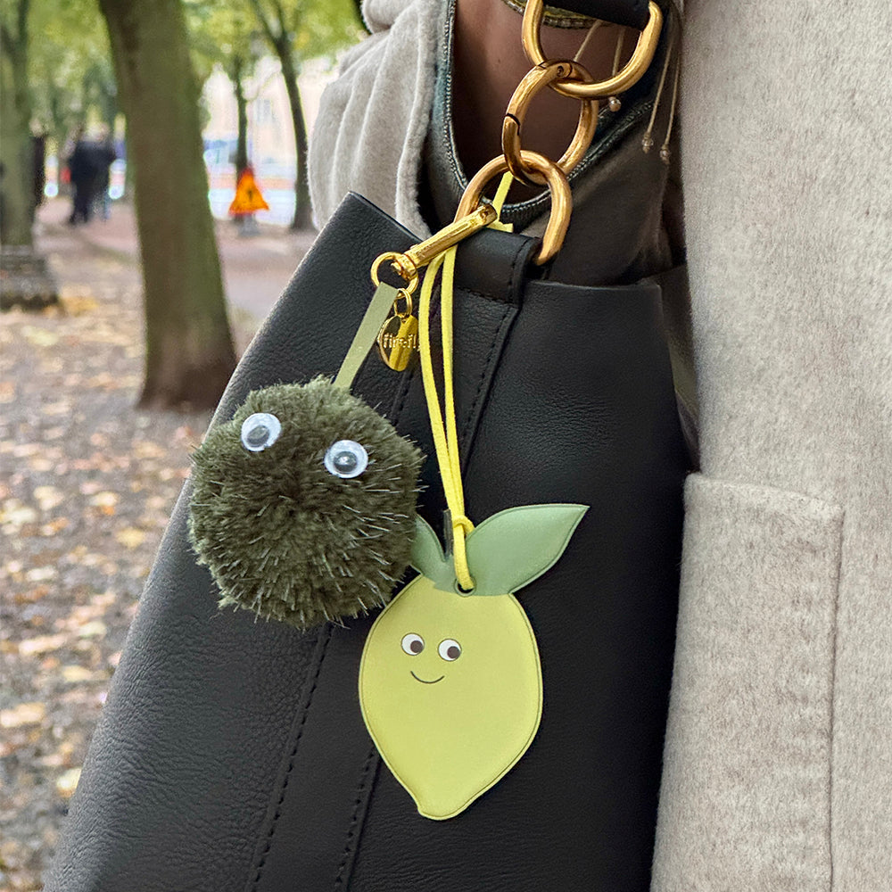 Keychain with a green pom-pom and lemon-shaped bag charm.